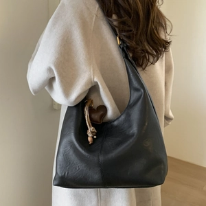 Detail of black leather hobo bag featuring a brown heart charm and woven strap on model