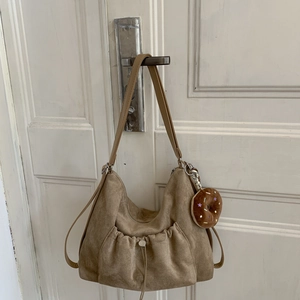 Detalle de bolso hobo de ante caqui con bolsillo de cordón y colgante de donut de felpa en puerta