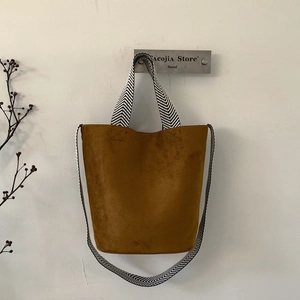Close-up of brown suede bucket bag featuring contrast herringbone patterned strap