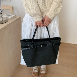 Detail einer großen schwarzen Canvas-Tasche mit Metallösen und dekorativem Gürtelriemen