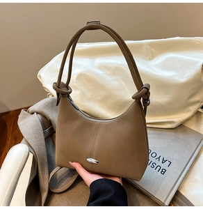 Detail of light brown Boston bag with knotted strap and oval silver metal logo plaque