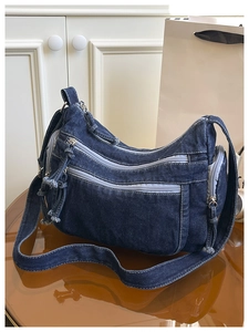 Detailed view of the dark blue denim crossbody bag with multiple zippers and half-moon shape