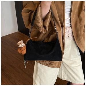 Detail of black large capacity underarm bag with a brown teddy bear charm on model