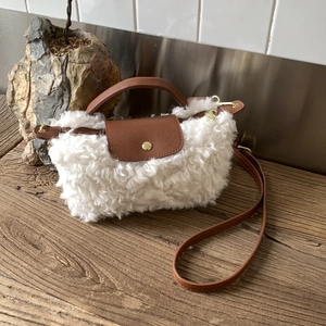 Detail of white faux shearling handbag with brown leather flap and gold metal snap buckle