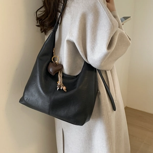 Close-up of black leather hobo bag with heart charm and woven tassel details