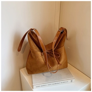 Détail d'un sac cabas en daim marron avec un nœud en cuir posé sur un livre d'art