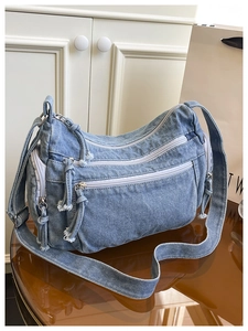 Detailed macro view of the blue denim shoulder bag showing white zippers and fabric texture