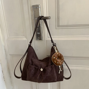 Detalle del bolso hobo de ante marrón oscuro con un llavero de donut de felpa en una puerta