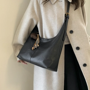 Detail of black leather hobo bag featuring heart charm and adjustable shoulder strap