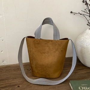 Detailed view of brown suede bucket bag with black and white herringbone patterned strap