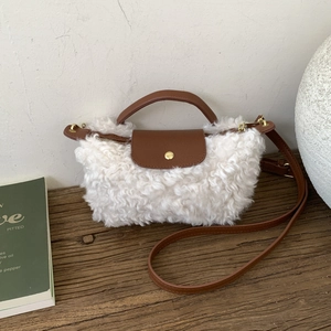 Detail of white plush crossbody bag featuring brown leather trim and gold snap button