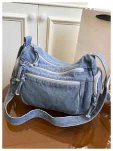 Detailed view of denim crossbody bag with multi-pocket structure and tassel zippers