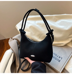 Detail of minimalist black matte crossbody bag with silver oval metal hardware and knot strap