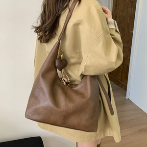 Detail view of large brown faux leather hobo tote bag with heart charm and tassel decoration