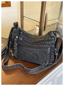 Detail of dark denim crossbody bag with multiple zippers on a wooden shop counter
