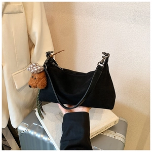 Close-up of minimalist black shoulder bag with a cute teddy bear plush charm detail
