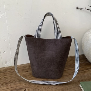 Detail of dark faux suede bucket bag featuring black and white chevron patterned strap