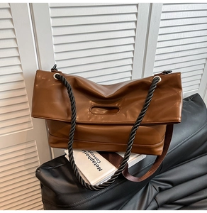 Detail of a brown leather shoulder bag featuring a black thick spiral woven rope strap