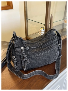 Detail of dark grey washed denim crossbody bag with multiple zippers and fringe tassels