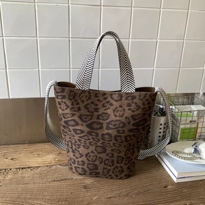 Detail view of leopard print bucket bag featuring woven herringbone straps on a wood surface