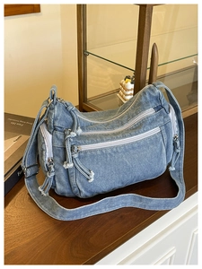 Detail of blue denim crossbody bag featuring triple zipper compartments and adjustable strap