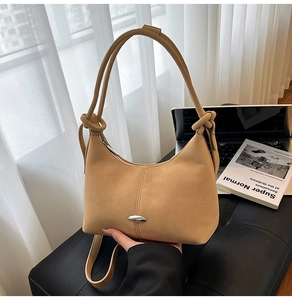 Close-up of tan hobo bag featuring silver oval hardware and knotted strap on soft leather