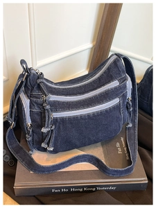 Detailed view of dark blue denim crossbody bag with multiple zippers and washed texture