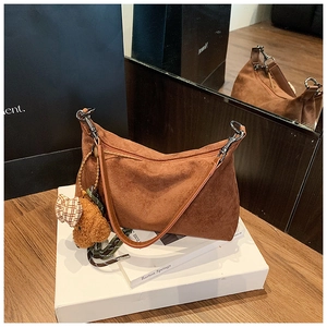 Detail of brown faux suede shoulder bag featuring a bear charm and braided rope accent