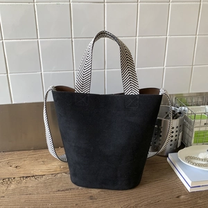 Detail of black suede bucket bag featuring woven herringbone handle on wooden table