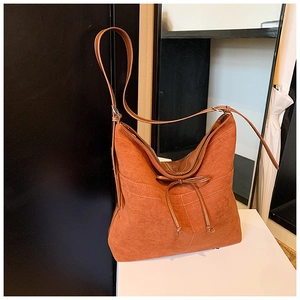 Détail du sac bandoulière en daim orange-brun avec nœud en cuir et surpiqûres blanches