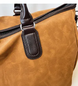 Vue détaillée de la texture daim marron mat et de la poignée en cuir du sac fourre-tout