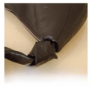 Close-up of dark brown leather handbag with knotted handle detail and silver metal zipper
