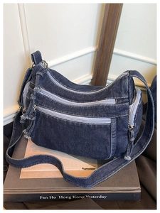 Detail of vintage denim crossbody bag featuring multiple front zippers and washed texture