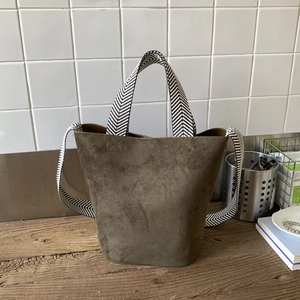Detailed view of an olive green suede bucket bag featuring a woven herringbone strap