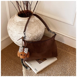 Detailed view of brown suede handbag with a plush teddy bear charm on a woven stool
