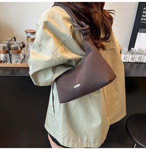 Detail of dark brown matte leather shoulder bag with knotted strap and oval metal accent