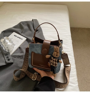 Detail view of denim bucket bag with leather accents and floral woven shoulder strap
