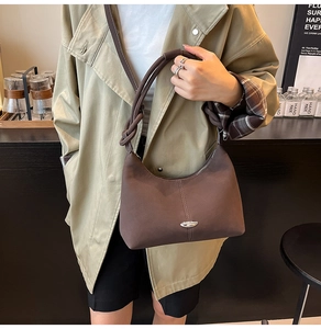 Detail of vintage brown underarm bag featuring a unique knotted handle and metal logo plaque