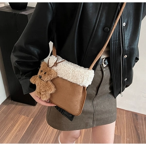 Detail of brown suede crossbody bag with plush white trim and a cute teddy bear charm
