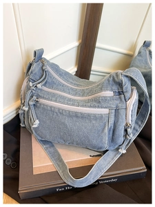 Detail view of light blue denim crossbody bag with multi-zipper pockets on vintage books