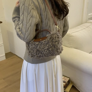 Close-up of grey faux shearling handbag with brown leather strap and handle detail