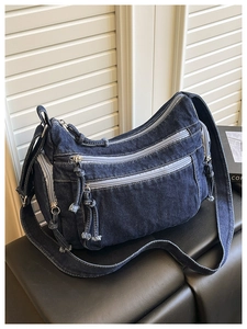 Detail of blue denim crossbody bag featuring multiple zipper pockets and woven pullers