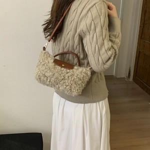 Detail of plush beige crossbody bag with brown leather accents on a knitted sweater
