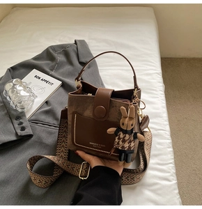 Brown bucket bag detail with textured strap and cute bunny charm on grey blazer