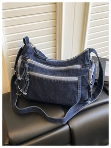 Detail view of dark blue denim crossbody bag featuring multiple functional zipper pockets