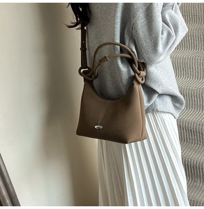 Detail view of coffee brown leather bag with knotted strap and metal logo on strap