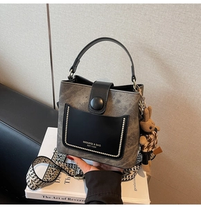 Close-up of retro gray bucket bag with black leather flap and geometric woven strap