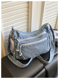 Detail of light blue denim crossbody bag with multiple zippers and adjustable strap