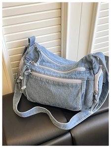 Close-up of light blue denim crossbody bag with multiple pockets and silver zippers