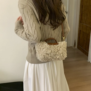 Detail of beige faux fur handbag featuring brown leather handles and gold metal hardware